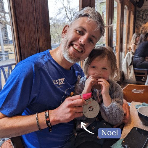 Noel showing his race medal to a young girl, both smiling.