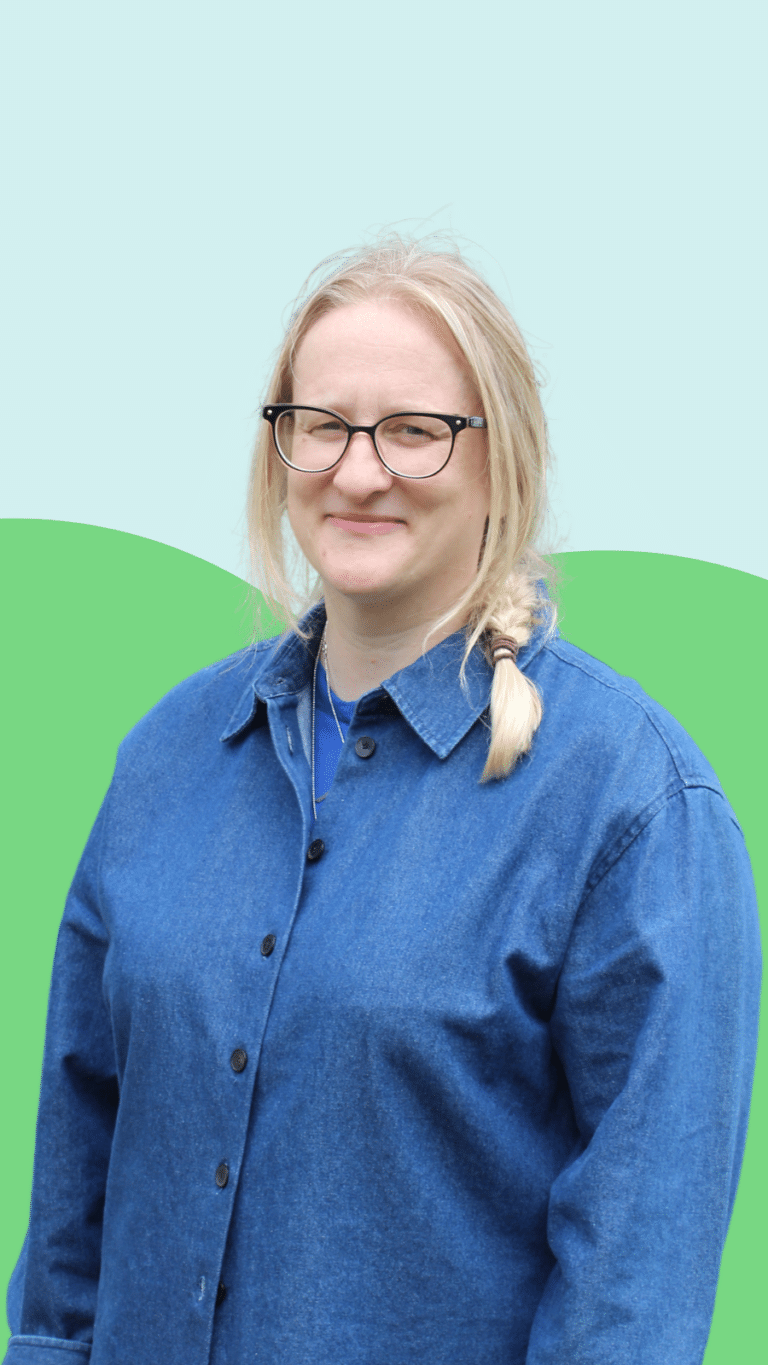 Photo of Penny Brohn UK Trustee, Bronwen - a caucasian woman with light blonde hair, wearing black rimmed glasses and wearing a denim shirt.